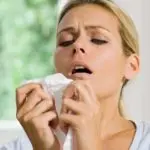 Woman holding a tissue with a distressed expression in a soft indoor setting, emphasizing HVAC-related allergy season issues.