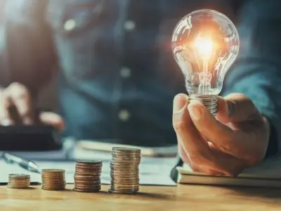 Light bulb symbolizing energy efficiency and savings held above stacked coins, representing lower energy bills and cost-effective heating and cooling solutions.