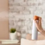 A hand holds a white aerosol spray can with an orange cap in a neutral interior, showcasing HVAC cleaning maintenance tips.