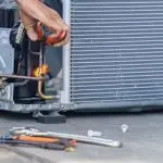 Hand repairing a refrigeration unit with tools and copper tubing, showcasing technical skill in HVAC work.
