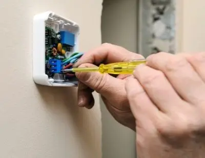 Person using a screwdriver to install a programmable thermostat, highlighting HVAC technology for energy savings in home heating.