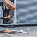 Technician repairing refrigeration unit outdoors with tools for HVAC service in Daytona Beach.