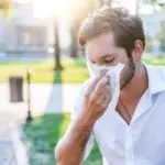 Man outdoors wiping his face with a tissue; bright day, related to Jerry Brittingham A/C & Heat, Inc. HVAC services.