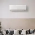 Wall-mounted air conditioner in a modern living space with cushions and a potted plant, by Jerry Brittingham A/C & Heat, Inc.