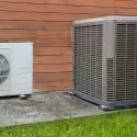 Air conditioning units on concrete base with grass, showcasing a compact white unit and larger gray metallic unit.
