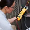 Female technician in safety glasses using a multimeter for HVAC electrical testing at Jerry Brittingham A/C & Heat, Inc.