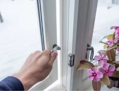 Hand opening a window with a potted flower nearby, illustrating the benefits of circulating fresh air to improve indoor air quality and reduce allergens.