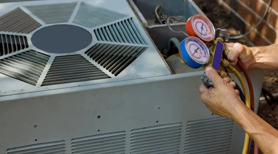 Hands holding refrigerant gauges connected to an air conditioning unit, illustrating the process of diagnosing refrigerant leaks and maintenance.