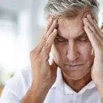 Middle-aged man with gray hair sitting indoors, hands on head, showing stress related to HVAC issues.