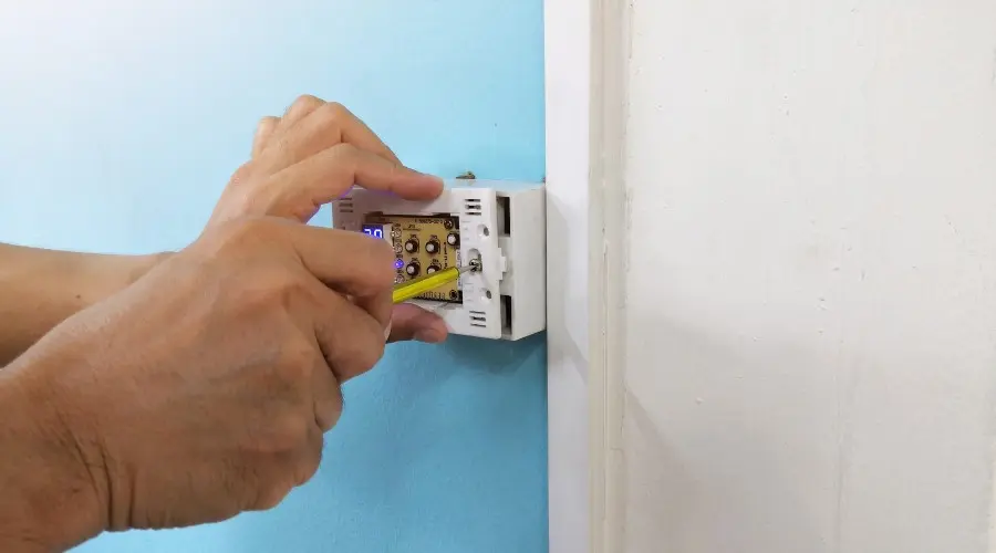 Person adjusting a thermostat on a blue wall, illustrating the process of thermostat replacement and upgrades for improved HVAC efficiency.