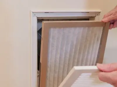 Person replacing an air filter in a home HVAC system, highlighting the importance of air filter maintenance for improving indoor air quality and reducing health risks.