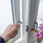 Hand reaching for window handle in bright room, potted orchid nearby, symbolizing HVAC comfort and indoor air quality.
