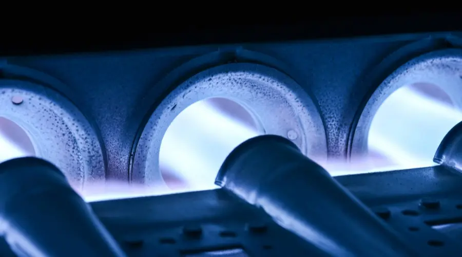 Close-up of furnace burners emitting blue flames, highlighting components at risk of overheating, relevant to furnace maintenance and safety.