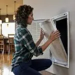 Woman with curly hair cleaning HVAC vent cover in modern kitchen, showcasing Jerry Brittingham A/C & Heat, Inc.'s expertise.