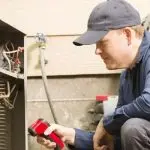 Man in navy jacket repairs equipment with red tool in HVAC setting, showcasing Jerry Brittingham A/C & Heat expertise.