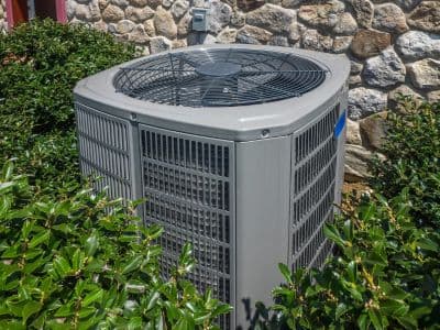 Central air conditioning unit surrounded by greenery, illustrating HVAC installation for effective cooling solutions in homes.
