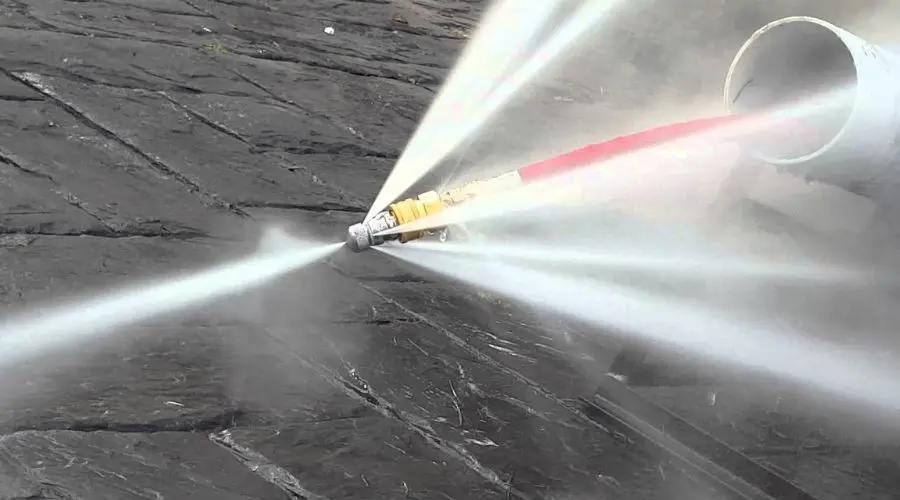 Hydrojetting equipment spraying high-pressure water to clear sewer line clogs, illustrating plumbing services related to drainage solutions.