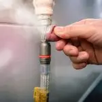 Hand adjusting a gas line connection with visible steam, illustrating gas line repair and safety measures related to gas leaks.