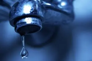 Leaking faucet with a drop of water forming at the spout, illustrating a common plumbing issue related to fixture leaks.