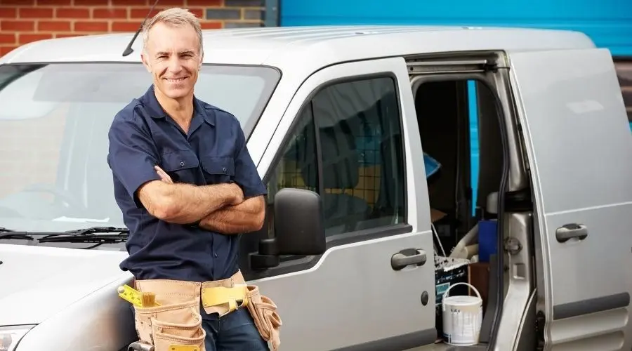Smiling plumber in uniform standing by service van with tools, representing The Plumbing Dr's emergency plumbing services.