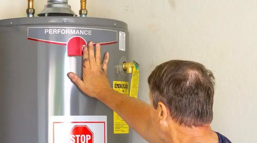 Man inspecting a water heater with a hand on the performance indicator, emphasizing maintenance and replacement signs relevant to plumbing services.