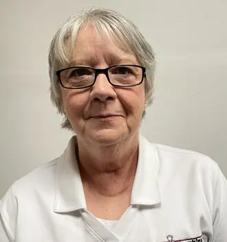 Melody, customer service representative at The Plumbing Dr, wearing a white polo shirt, with glasses and short gray hair, smiling against a neutral background.