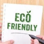 Hand holding a marker writing "Eco Friendly" on a notebook, emphasizing sustainable plumbing practices and water conservation.