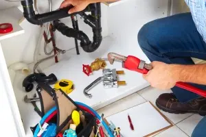 Plumber using tools for drain cleaning under a kitchen sink, showcasing plumbing repairs and maintenance.