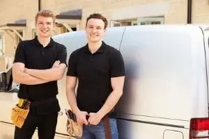 Two plumbers standing confidently beside a service van, wearing black polo shirts and tool belts, representing The Plumbing Dr's residential and industrial plumbing services.