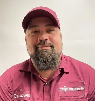 Dr. Harold, plumbing technician at The Plumbing Dr, wearing a maroon uniform with logo, smiling, showcasing expertise in plumbing services.