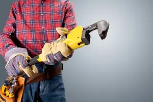 Plumber holding a large yellow pipe wrench, wearing gloves and a plaid shirt, emphasizing professional plumbing tools and readiness for service.