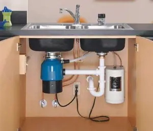 Garbage disposal unit installed under a kitchen sink, showcasing plumbing connections and maintenance components, relevant to garbage disposal repair services.