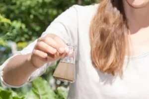 Person holding a glass flask with murky water, illustrating water quality issues related to plumbing and potential contamination.