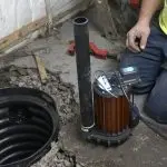 Sump pump installation in a basement with a technician preparing a primary pump next to a sump pit.