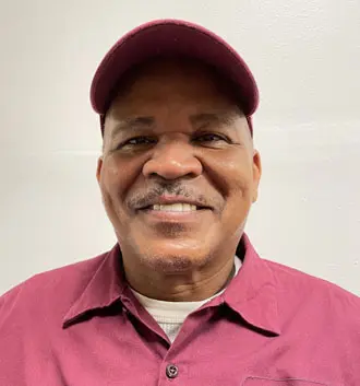Smiling plumber assistant in maroon uniform and cap, representing The Plumbing Dr team, emphasizing customer service and satisfaction.