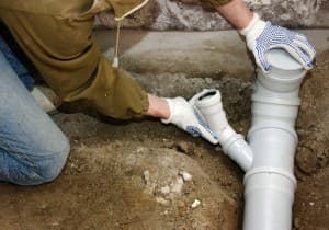 Person in gloves repairing a drain pipe, emphasizing proper drain maintenance techniques relevant to plumbing services.