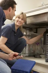 Plumber and customer discussing plumbing repair under sink, highlighting professional service for sewer line issues.