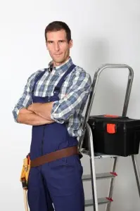 Professional plumber in work attire, standing confidently with arms crossed, toolbox and ladder in background, representing expert plumbing services for trenchless sewer repair.