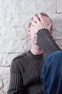 Man with head in hands, expressing distress, against a textured wall, reflecting the urgency and seriousness of addressing gas line leaks for family safety.