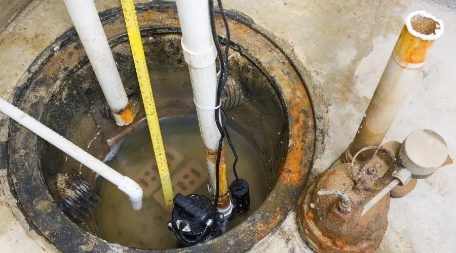 Sump pump installation in a basement pit with water and pipes, highlighting plumbing maintenance for homeowners.