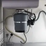 Garbage disposal unit installed under kitchen sink, showcasing plumbing connections and electrical wiring, relevant to repair and installation services offered by The Plumbing Dr in Falls Church, VA.