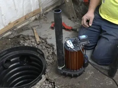 Sump pump installation next to sump pit, showcasing plumbing tools and worker's hands, emphasizing flood prevention for homeowners.