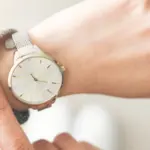 Hand wearing a silver mesh strap watch, showcasing a minimalist design with a white face and gold accents, illustrating the importance of time management in plumbing service scheduling.