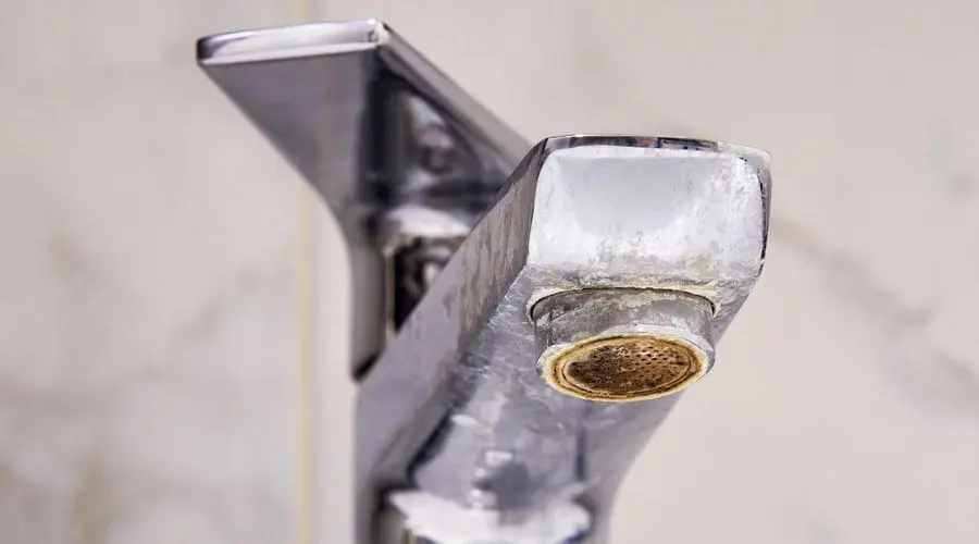 Close-up of a tarnished bathroom faucet showing mineral buildup, highlighting the need for plumbing maintenance to prevent issues during the holiday season.