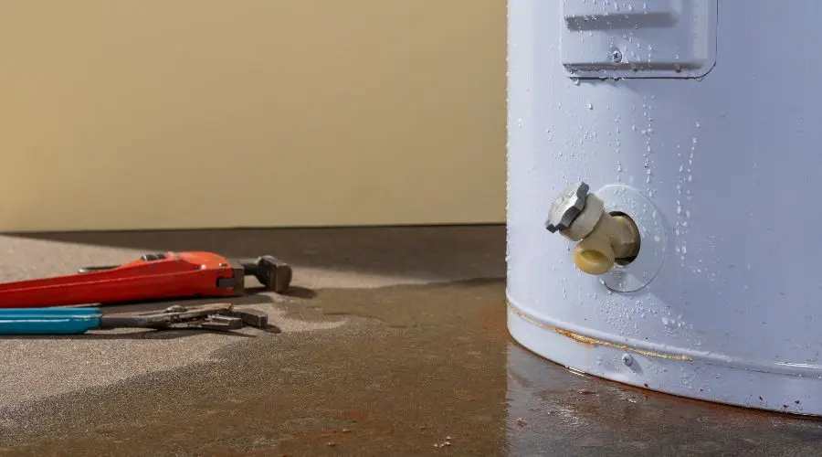 Water heater with visible valve and plumbing tools on wet floor, indicating potential leaks and need for replacement.