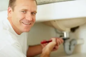 Arlington Plumber Smiling plumber working under a sink with tools, representing expert plumbing services in Arlington, VA.