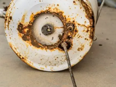 Corroded water heater tank showing significant rust and deterioration, indicating potential failure and the need for replacement.