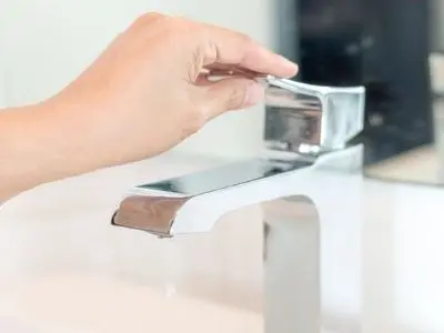 Hand turning off modern faucet, emphasizing water conservation tips for St. Patrick's Day gatherings.