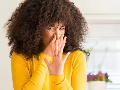 Woman in yellow sweater covering her nose, reacting to foul odor, indicating potential sewer line issue related to plumbing problems.