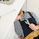 Plumber in uniform using a wrench to fix a plumbing issue under a sink, representing industrial plumbing services for commercial properties.